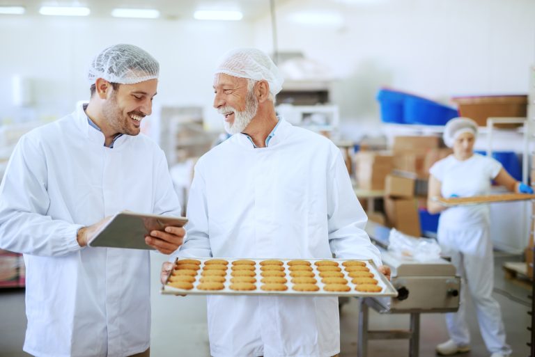 Senior adult employee holding tray with fresh cookies while supe